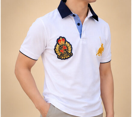 Weisses Poloshirt Kurzarm Herren – Frontansicht mit Wappen-Stickerei, Hand in der Hosentasche